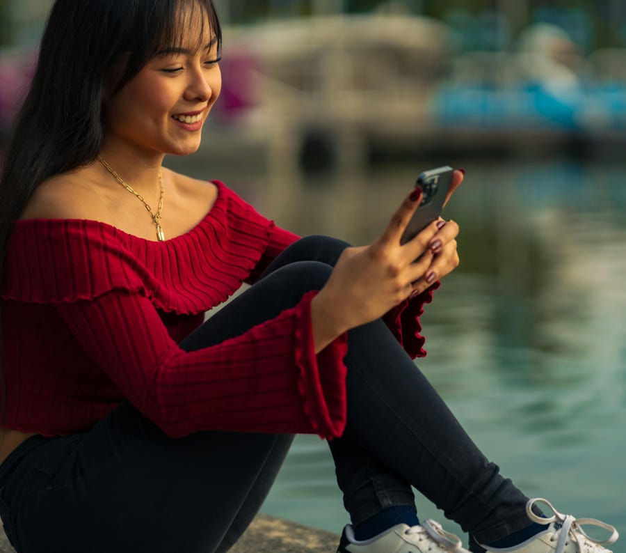 Lächelnde Frau sitzt an einem See und ist in ihr Smartphone in Mexiko-Stadt vertieft.